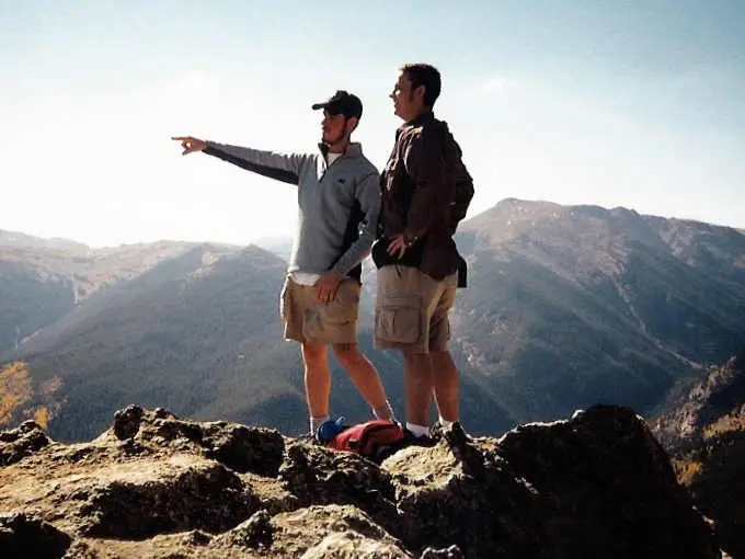 two friends on a mountain summit, one pointing into the distance