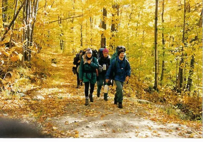 three friends with backpacks hiking a trail through yellow fall woods