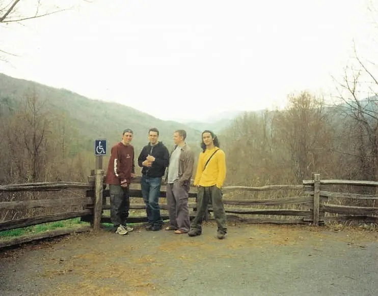four friends standing together at a fence on a mountain overlook in fall