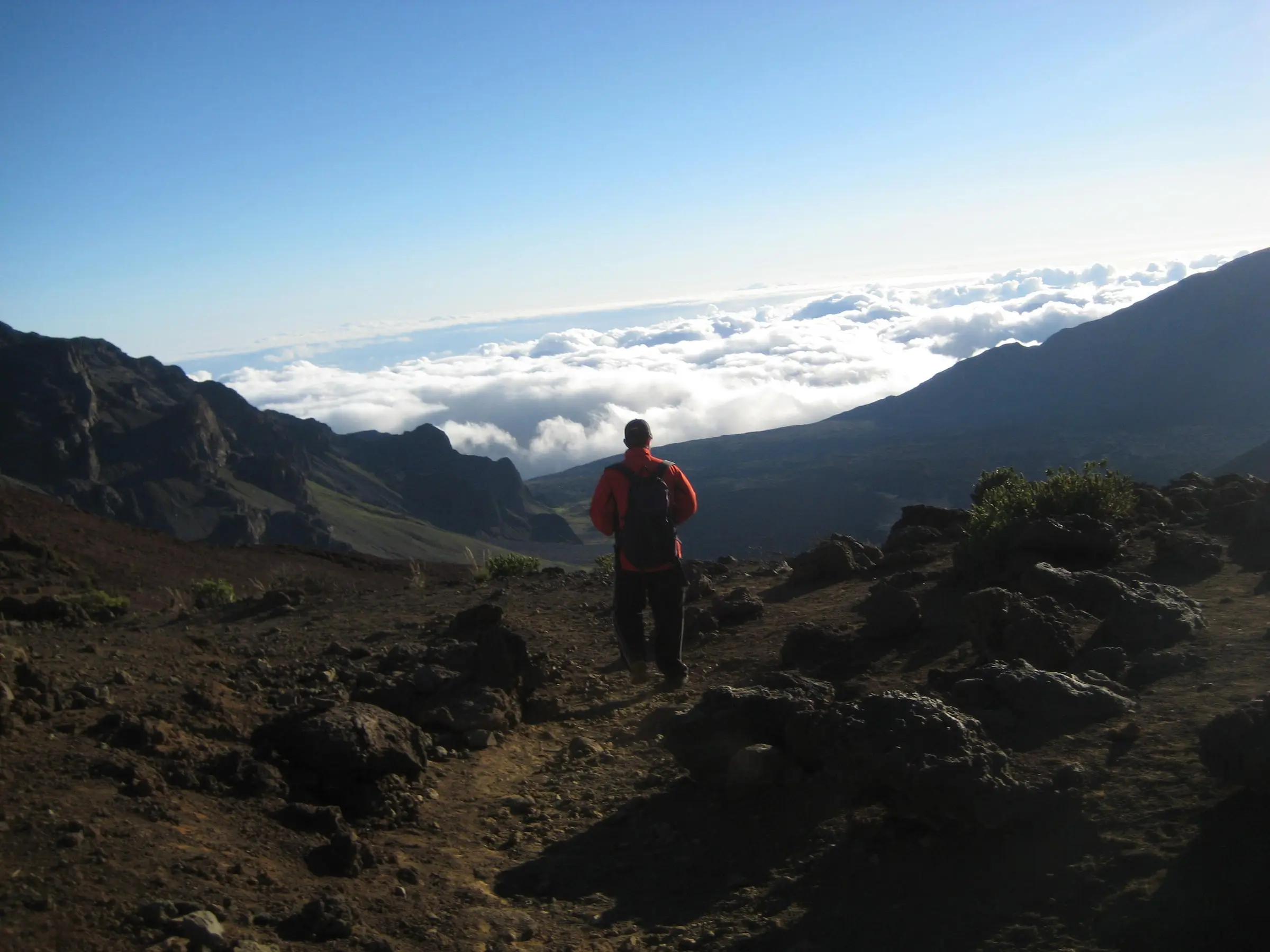 hiker walking down a rocky trail above the clouds