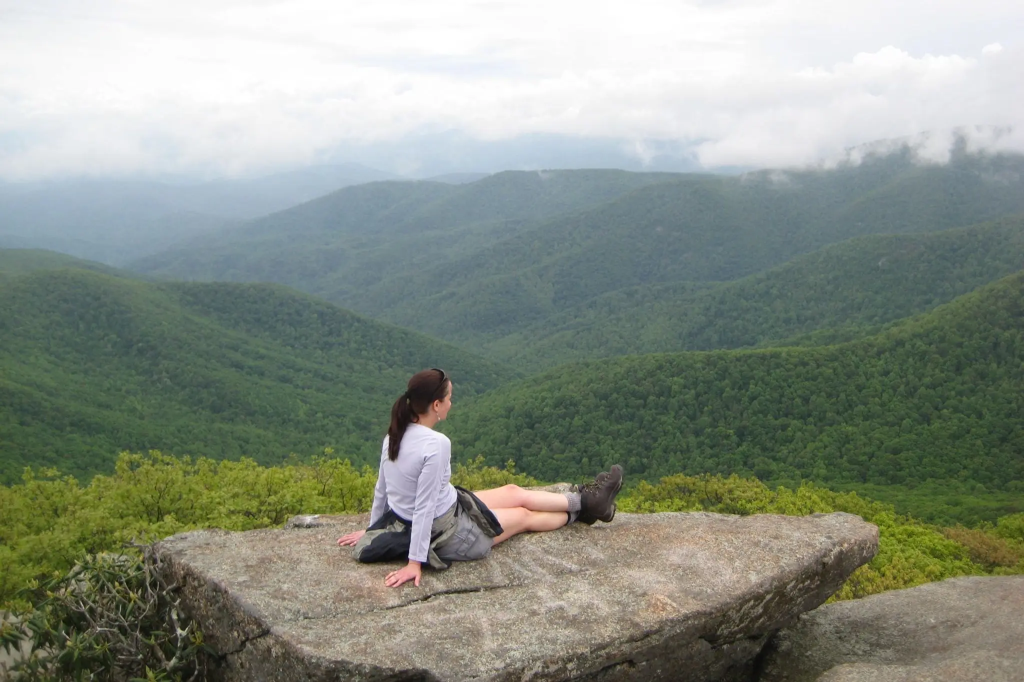 woman sitting on a rock looking out over green mountains