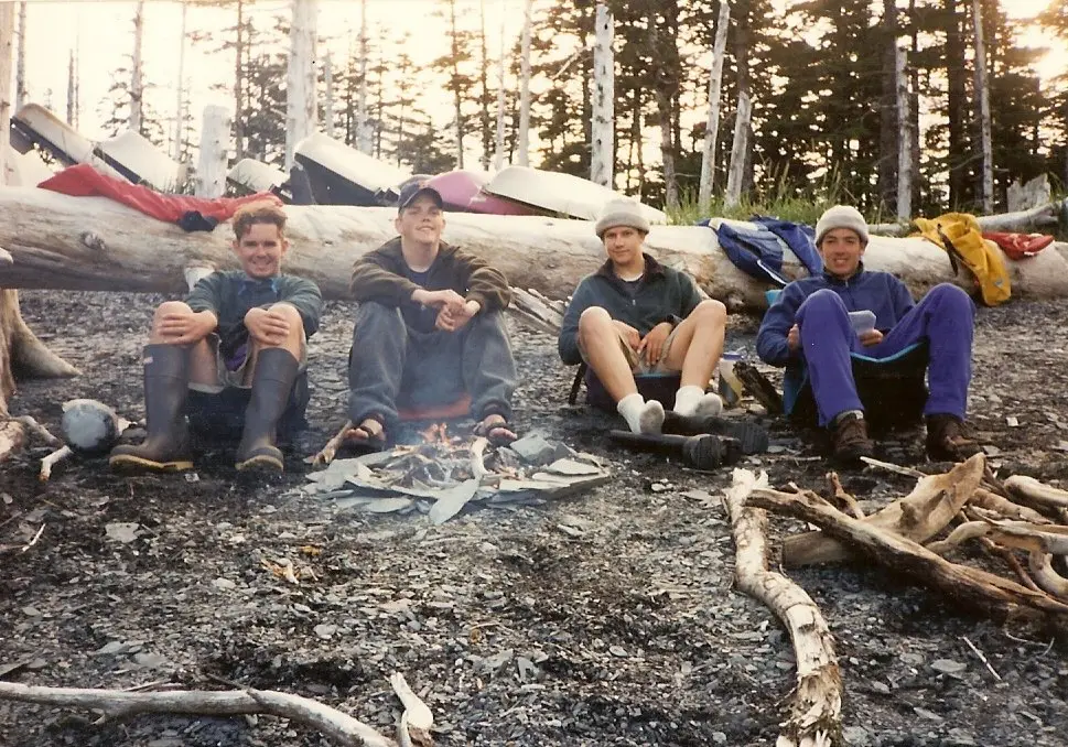 four friends sitting around a campfire on a rocky beach